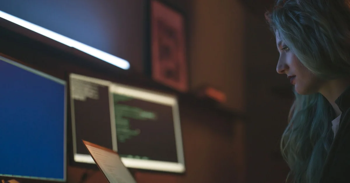 Programadora frente a varias pantallas con código en una oficina con poca luz
