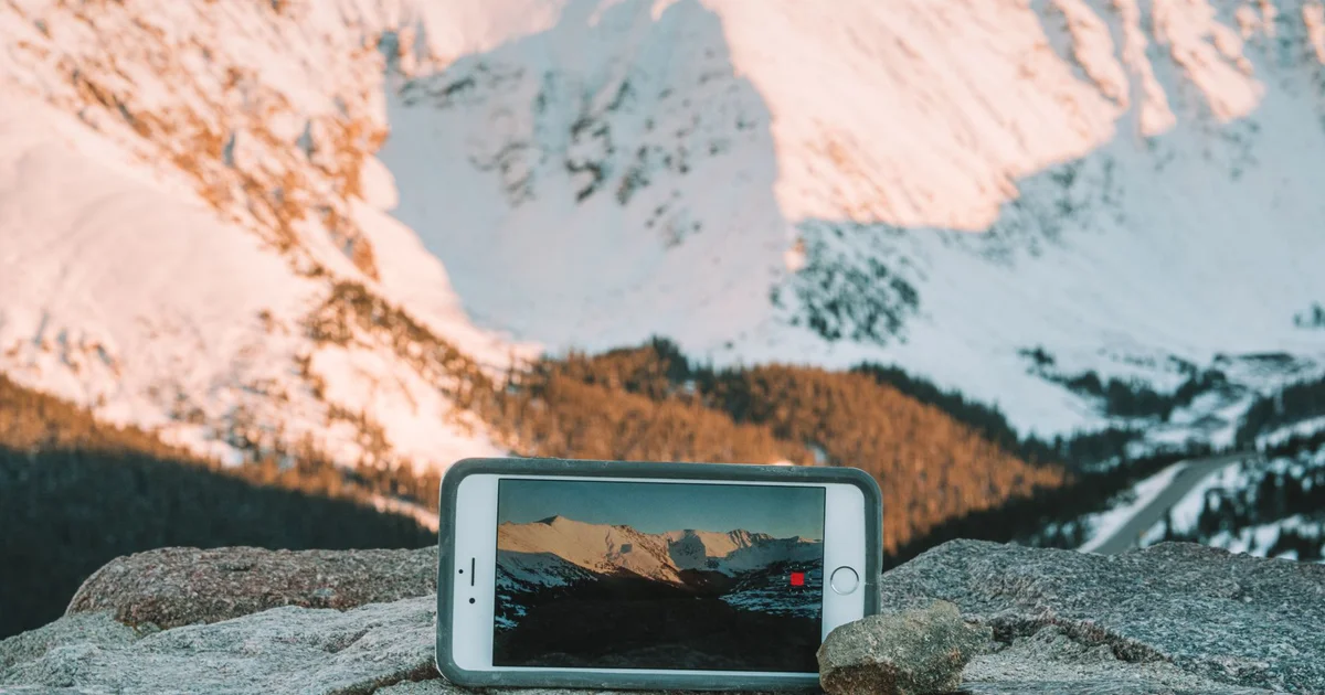Celular apoyado en una roca frente a montañas nevadas, en una zona remota sin ciudad cerca