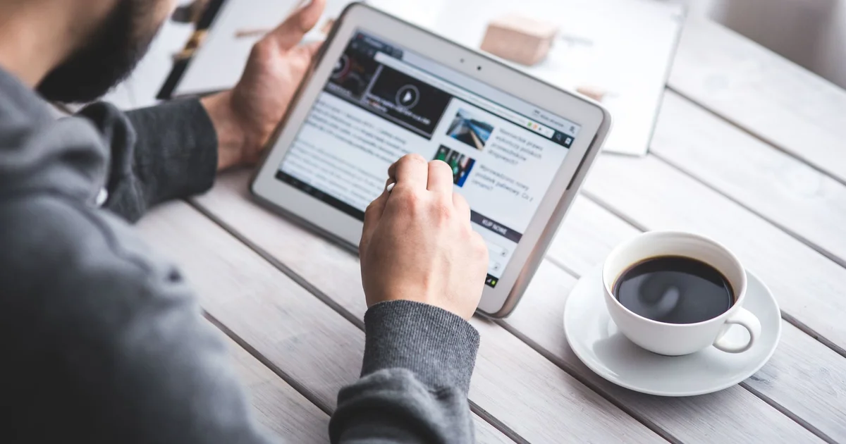 Hombre leyendo noticias en una tableta junto a una taza de café
