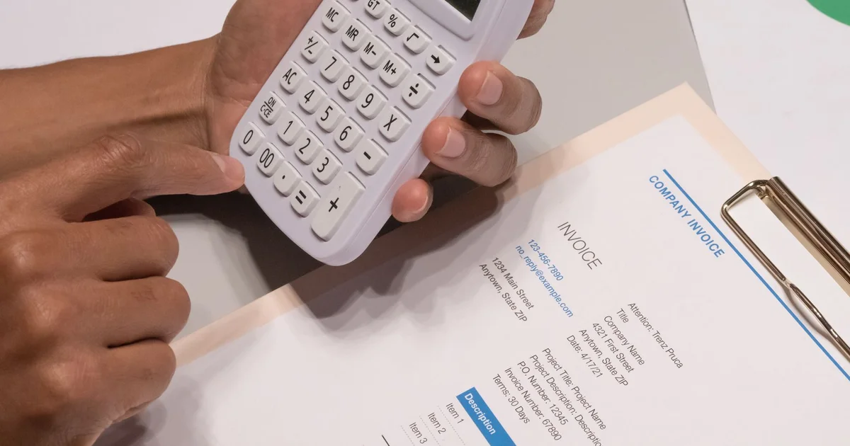 Manos usando una calculadora junto a una factura impresa sobre un portapapeles